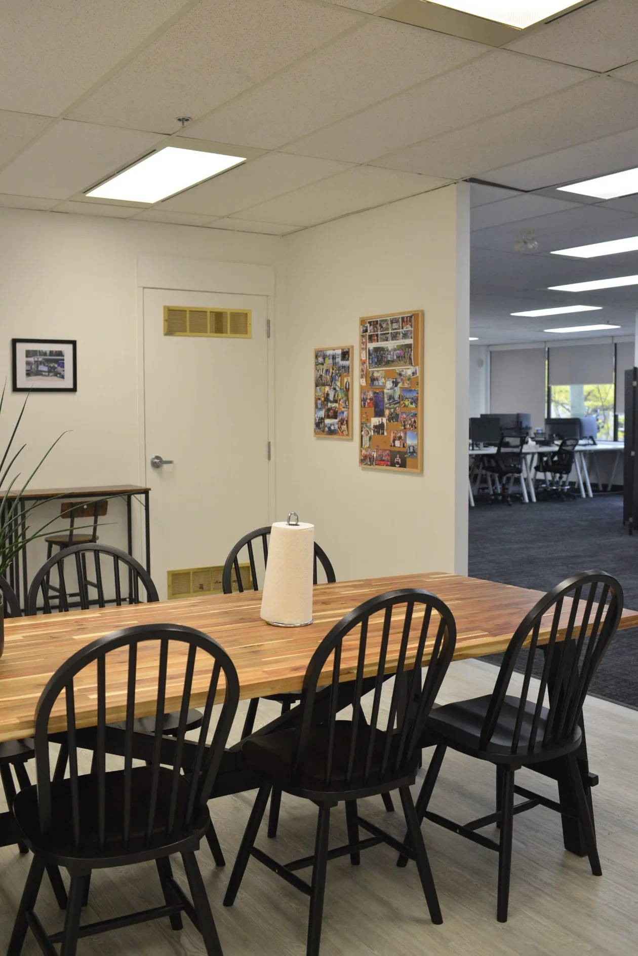 Lunchroom looking through to the open office, timber table and black chairs on plank flooring