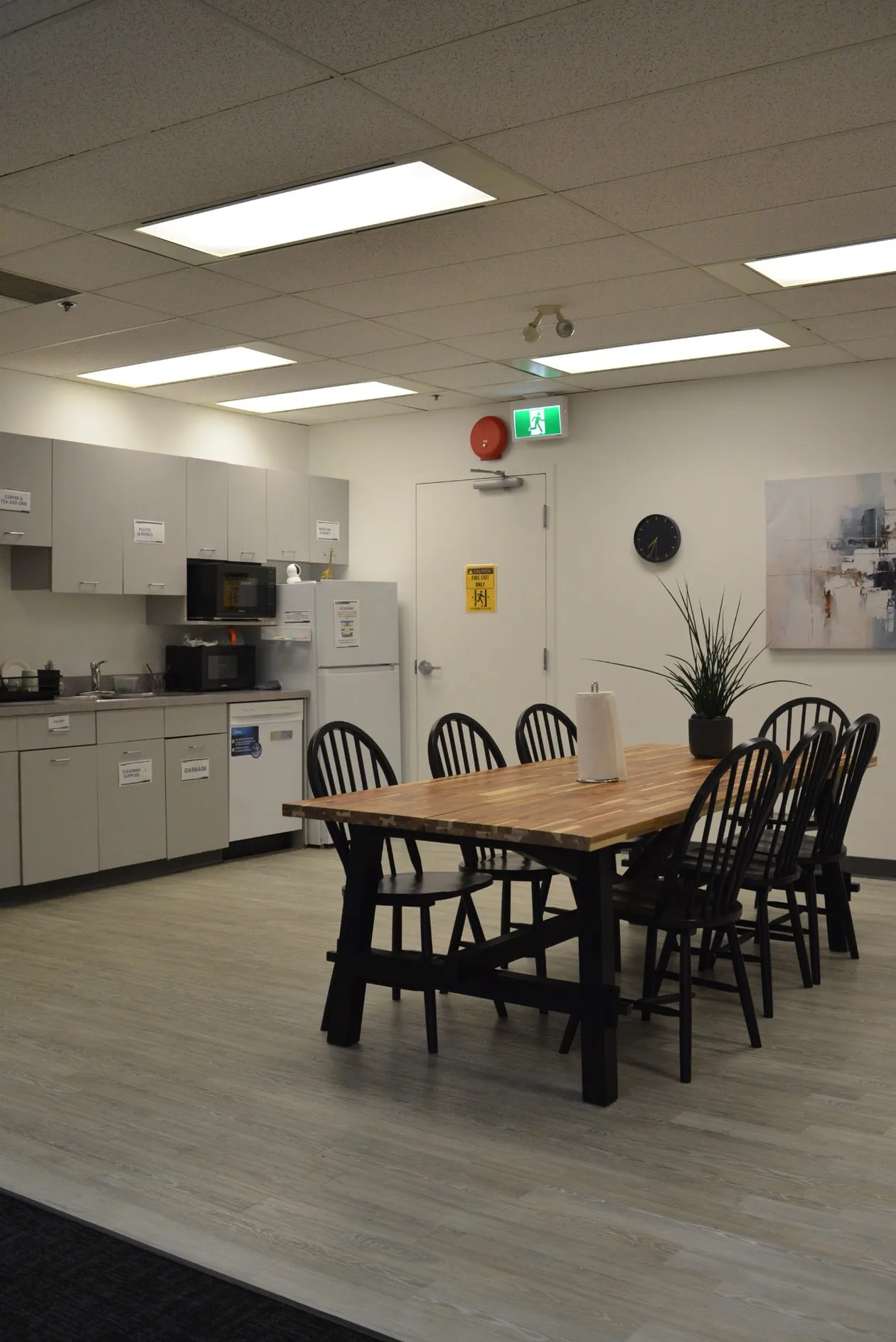 Blackbird Security Vancouver office fit-out — staff lunchroom with a solid timber table, black windsor chairs and a white kitchenette run