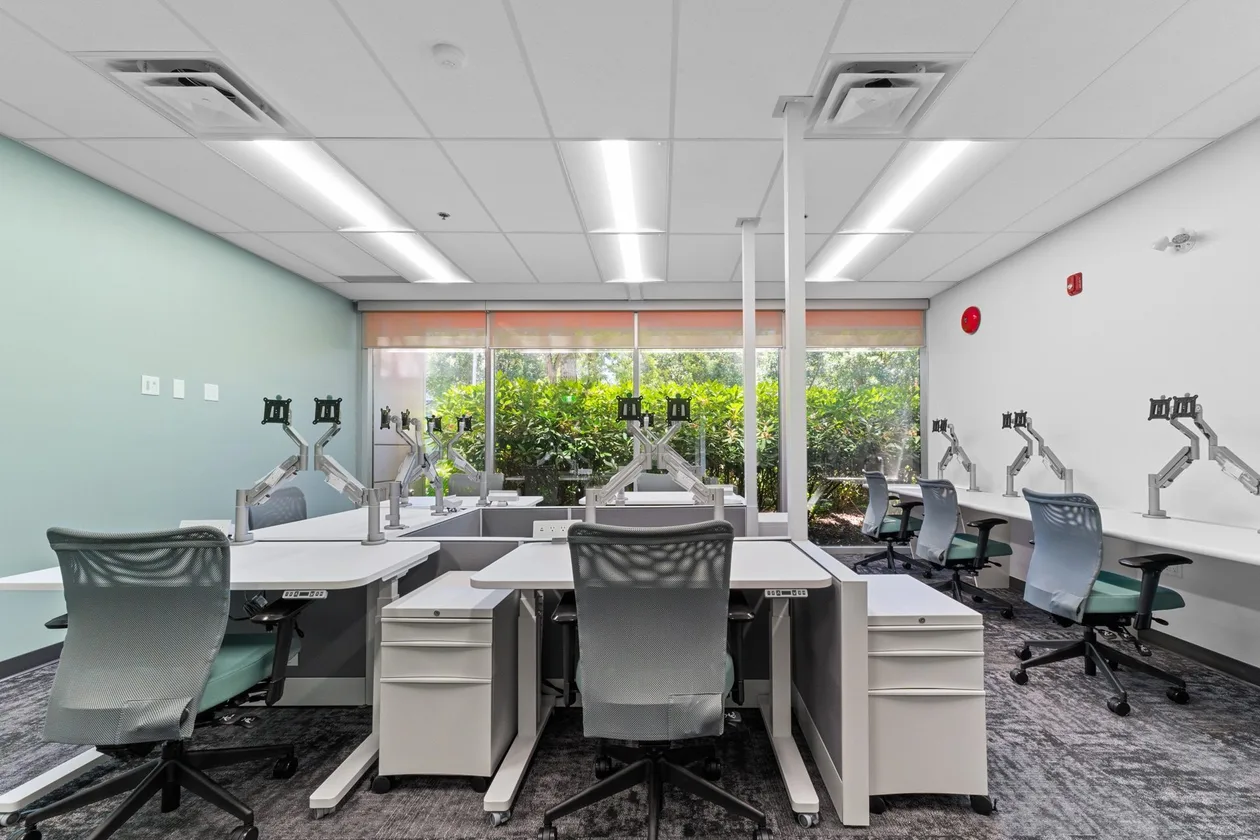 CFIA Burnaby accessibility upgrade — open workstation bench with monitor arms against a sage feature wall and window