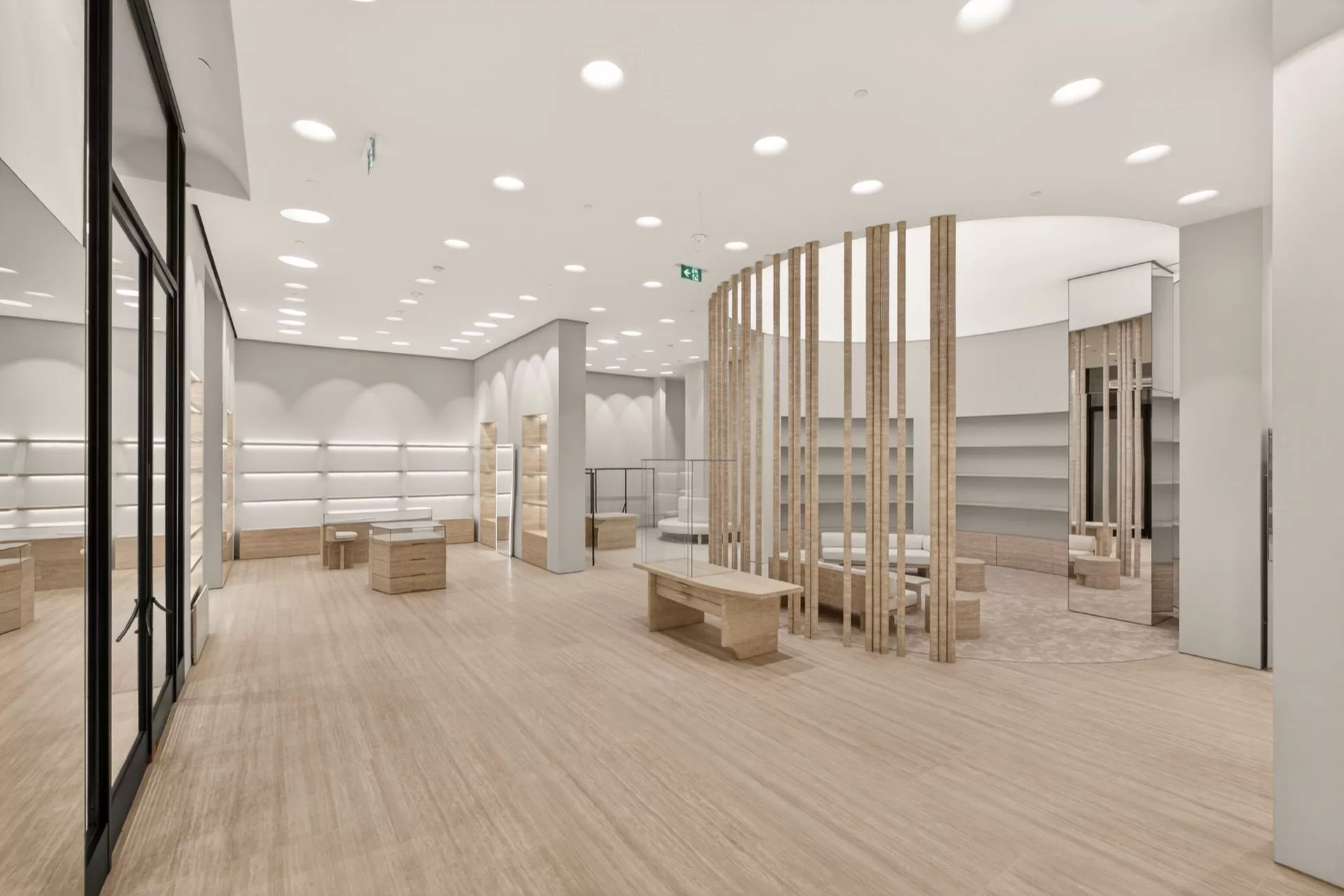 Curved fluted-slat fitting enclosure with a travertine bench and full-height mirrors on travertine plank flooring in a high-end retail boutique