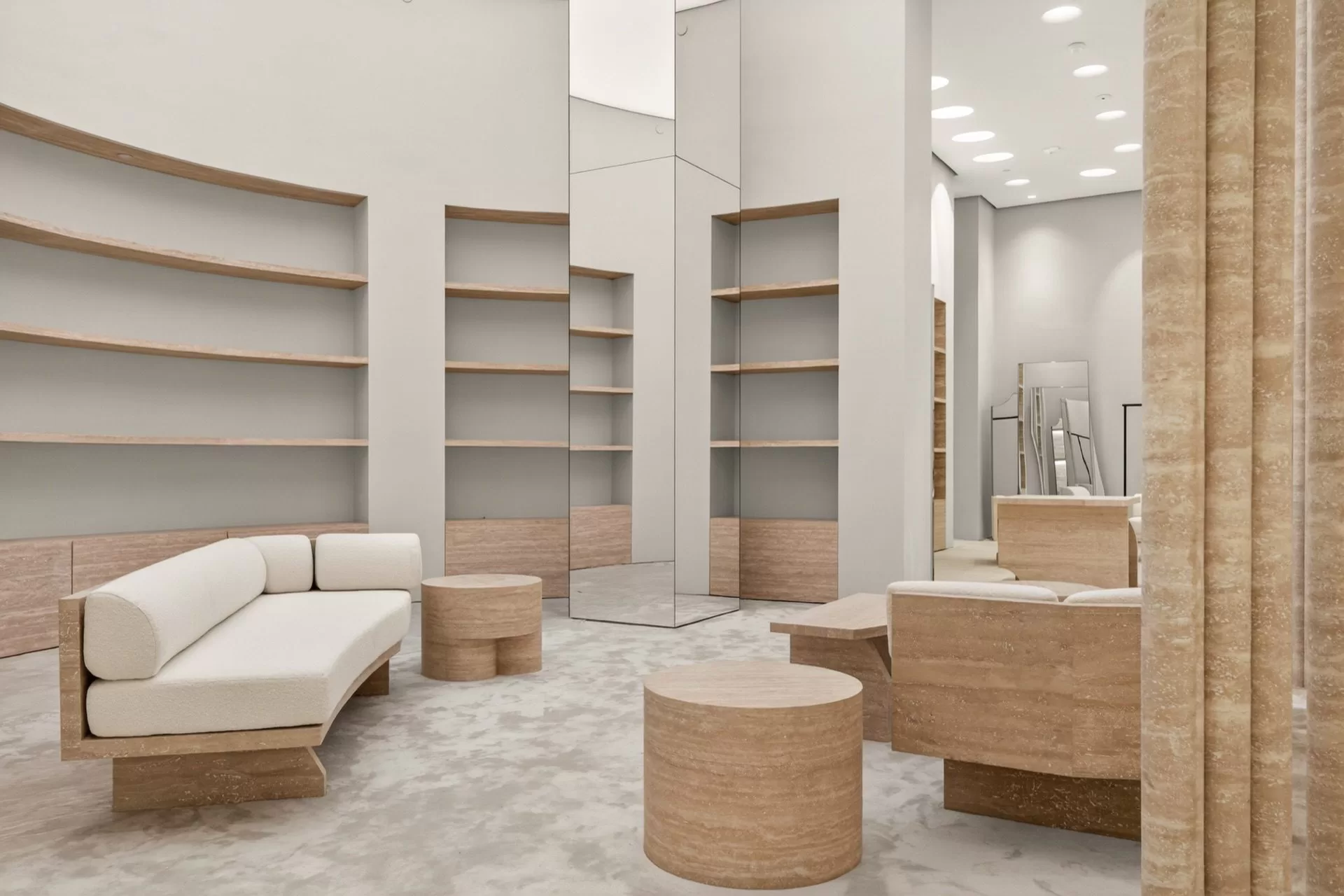 Maison Margiela fitting lounge — curved travertine shelving, a mirrored core column and bouclé upholstered seating in a luxury boutique fit-out
