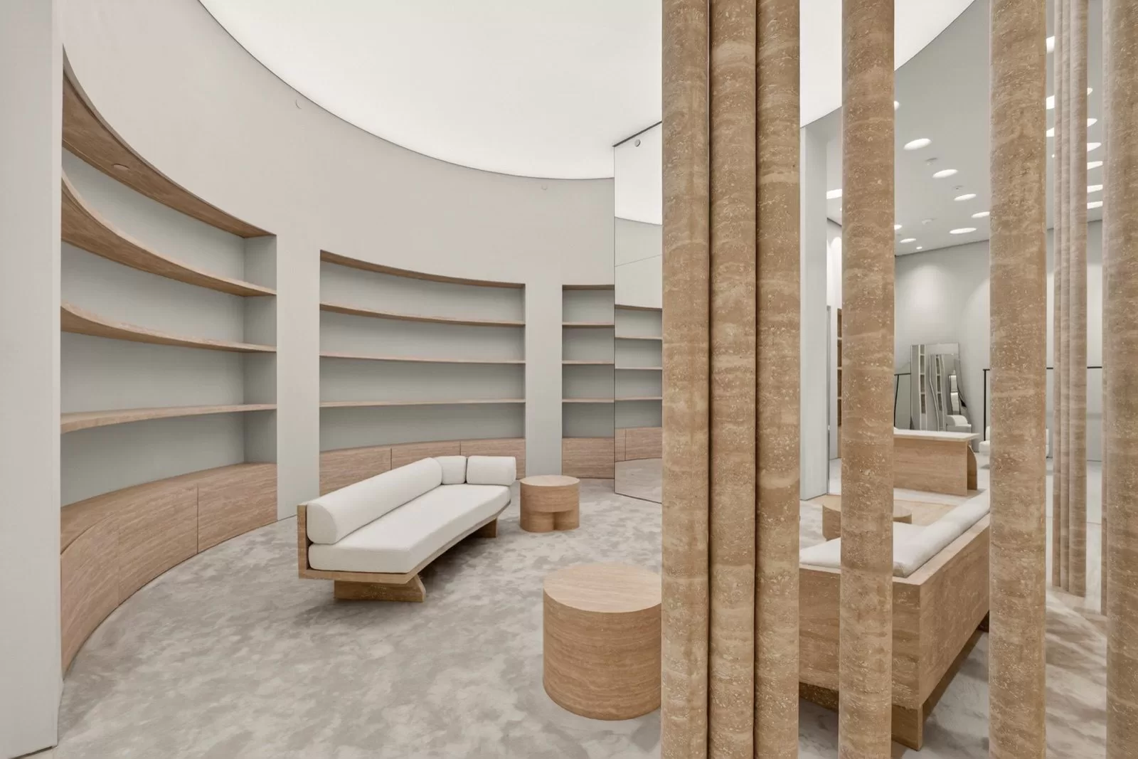 Maison Margiela circular fitting salon — sweeping curved travertine shelving, fluted travertine columns, a mirrored core and a bouclé settee, luxury boutique millwork and stonework, Oakridge Vancouver