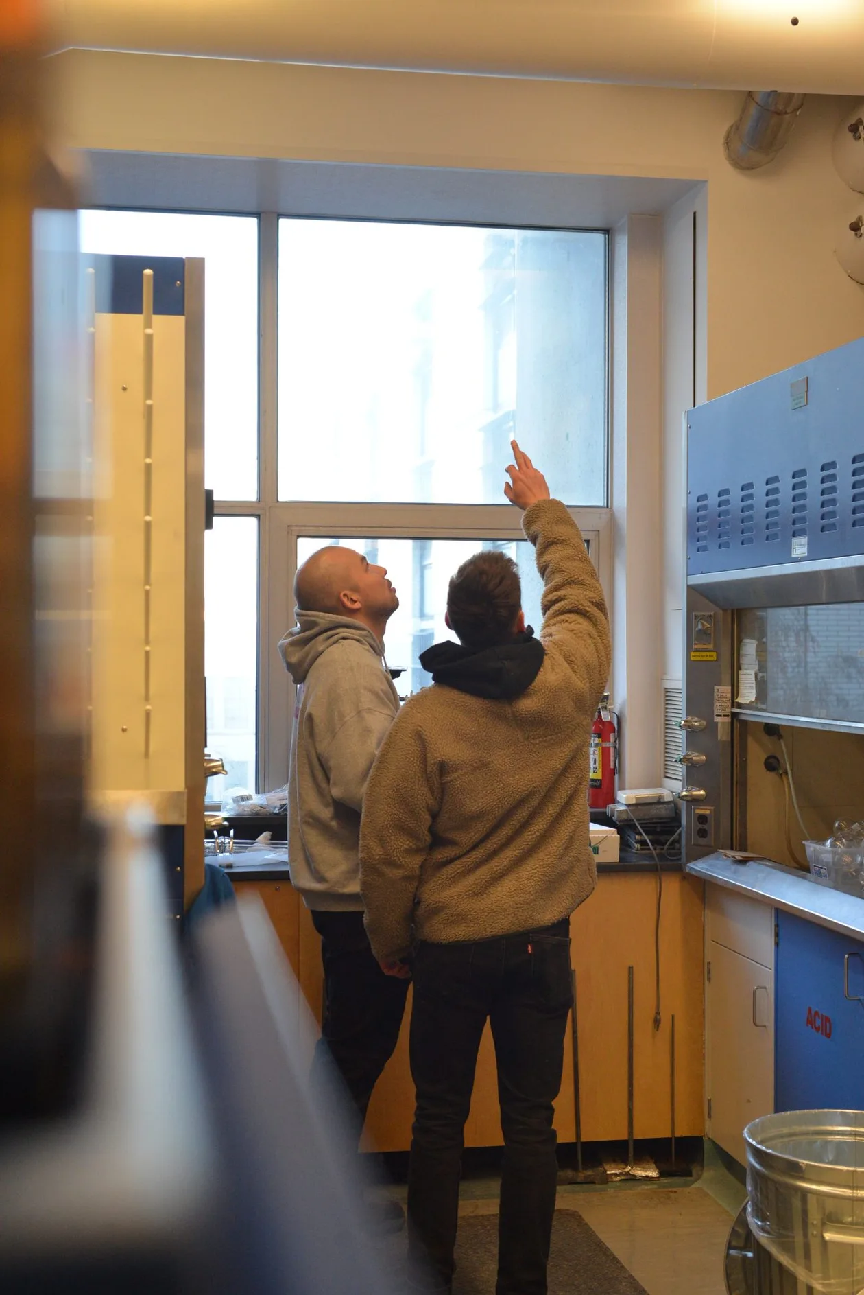 Two workers checking a window-mounted instrument in the chemistry lab