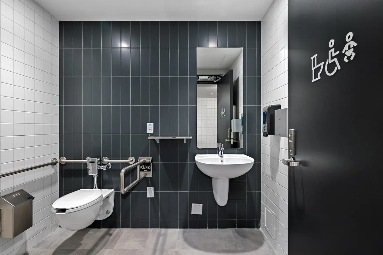 Accessible water closet with grab bars, dark tile and all-gender signage