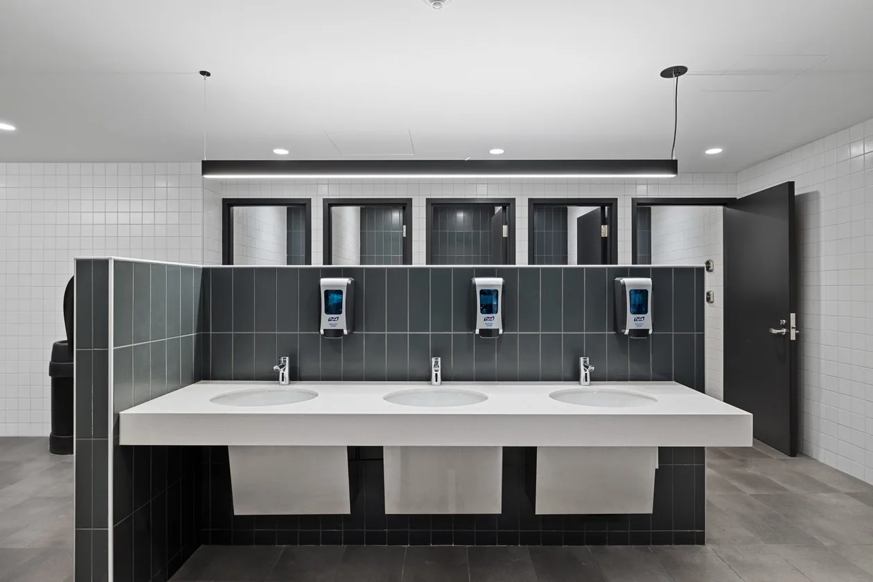 Vanity run with three basins, dark stack-bond tile, mirrors and a linear pendant