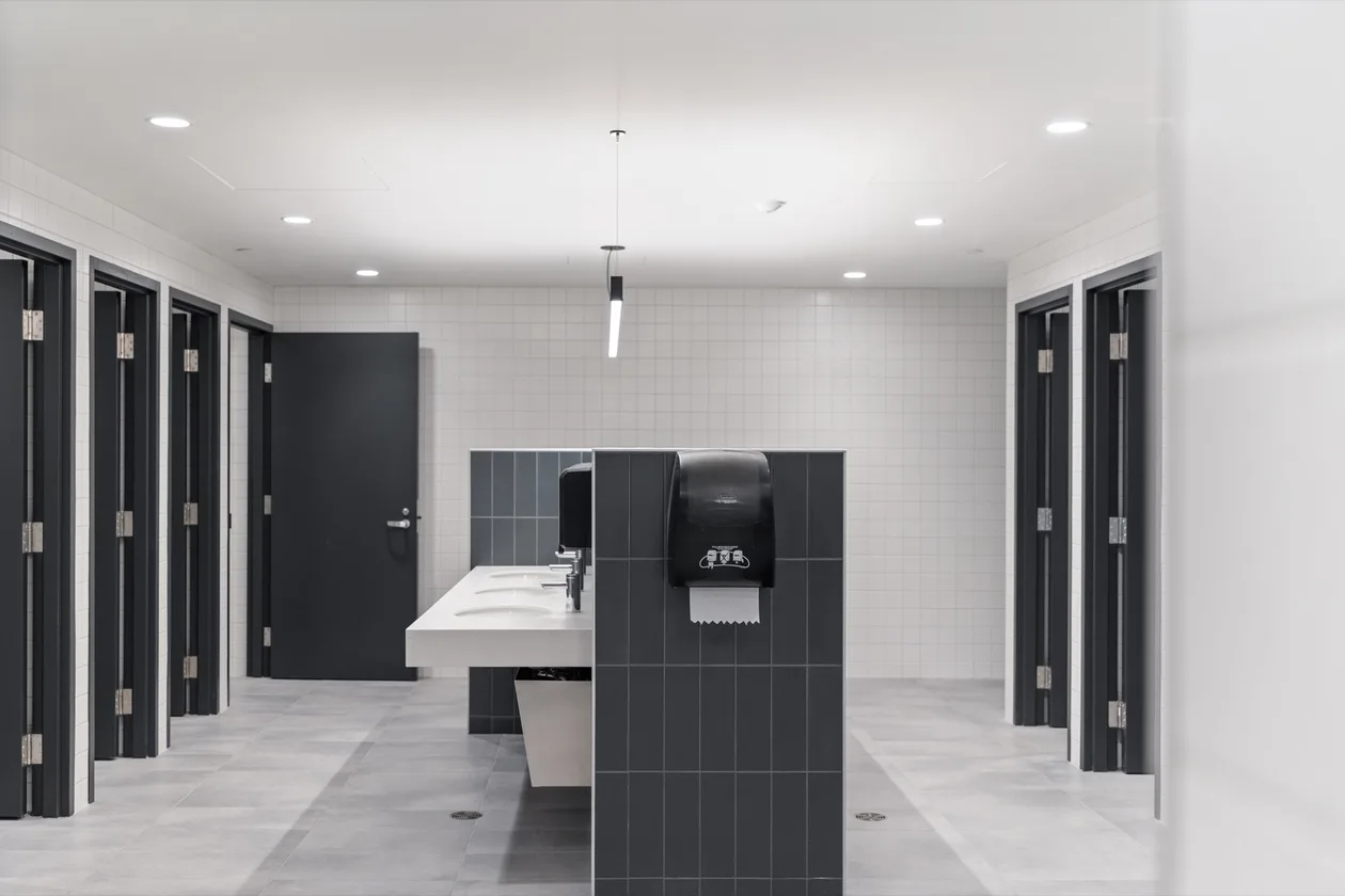 UBC Henry Angus all-gender washroom — solid-surface vanity with floor-to-ceiling dark stall doors