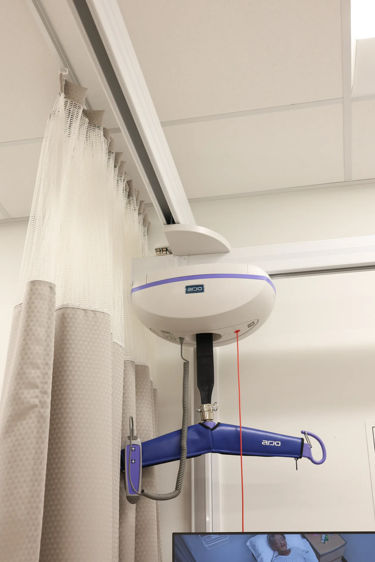 Ceiling-mounted patient lift on track beside the privacy curtain